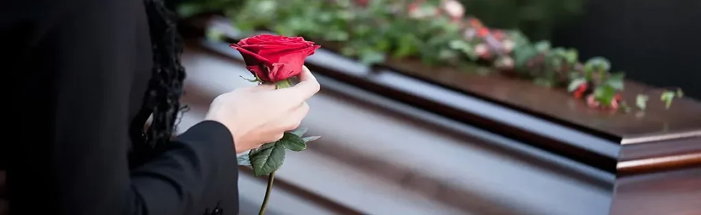 Proche tenant une rose rouge lors d'un dernier hommage devant un cercueil.