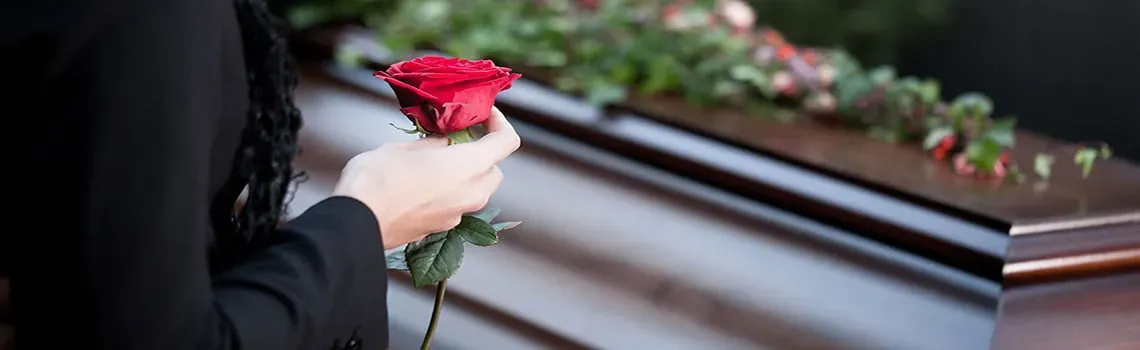 Proche tenant une rose rouge lors d'un dernier hommage devant un cercueil.
